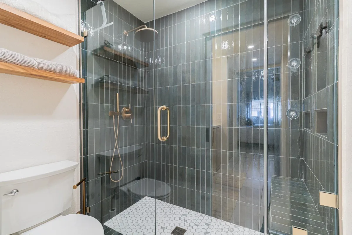 Teal vertical tile walk-in shower with brass fixtures